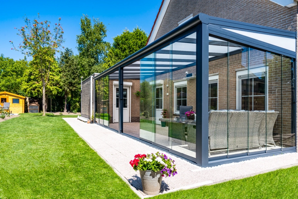 Zabudowany przeszklony ogród zimowy z metalową konstrukcją przy tarasie domu